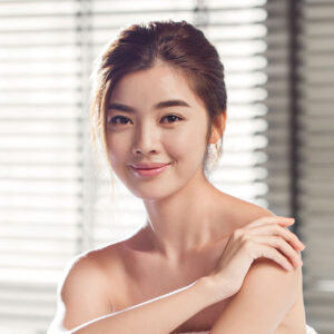 Young woman smiling and relaxing, showcasing confidence and beauty, in a serene spa-like setting, related to non-invasive body sculpting services.