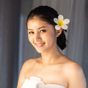 Smiling woman with a flower in her hair, wrapped in a towel, embodying relaxation and confidence, reflecting the essence of non-invasive body sculpting treatments at Superior Sculpting.