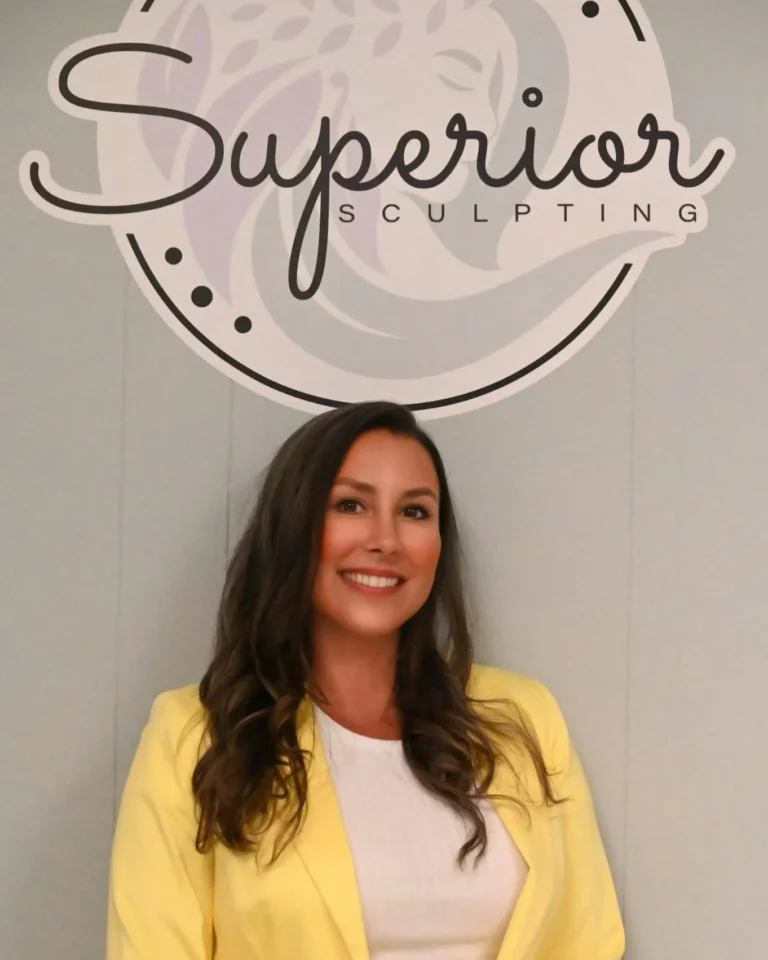 Ashley, founder of Superior Sculpting, smiling in a yellow blazer against the company logo, representing personalized non-invasive body sculpting services.
